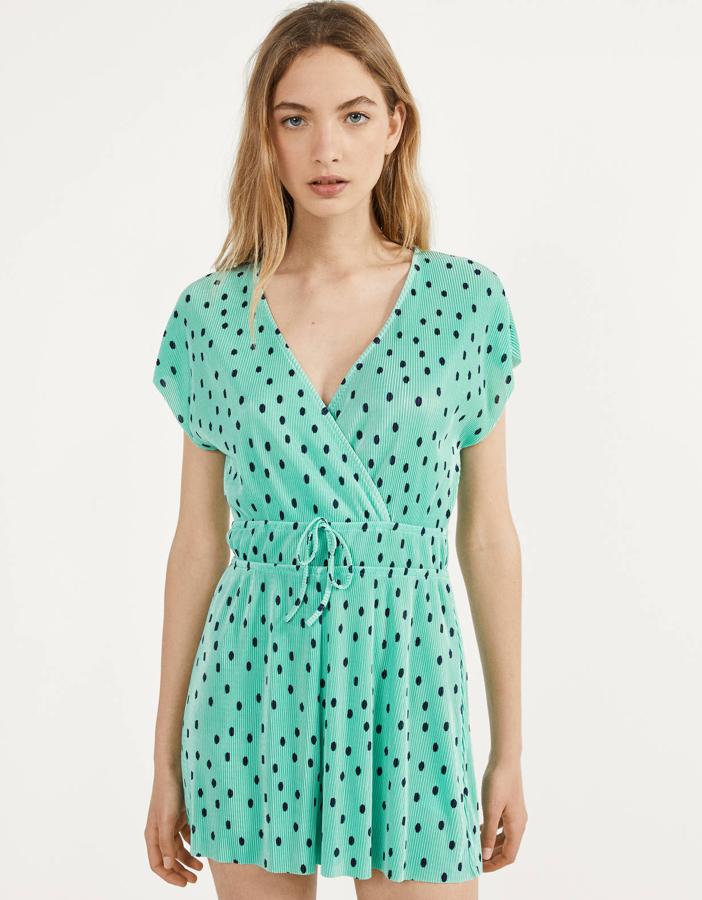 Este mono corto plisado sin mangas de color turquesa con topos en negro cuenta con escote en pico cruzado y cintura elástica. Tiene un precio de 12,99 euros.