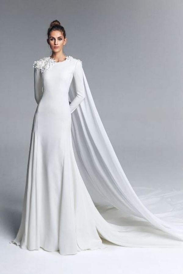 Vestido de novia realizado en crepe con cuello a la caja y manga larga. Cortes en el costado creando una falda de vuelo y bordado de flores de guipur en el escote y en la espalda con capa de gasa. Rebajado de 2.350 a 940 euros.