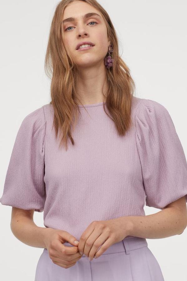 De corte recto en punto arrugado, esta blusa en color lavanda viene con cuello redondo, escote pronunciado en la espalda y mangas abullonadas fruncidas con elástico fino en los puños. Tiene un precio de 14,99 euros y está disponible entre las tallas XS y XXL.
