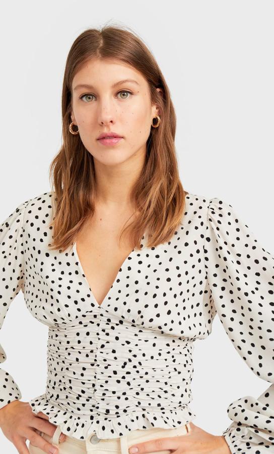 Blusa de escote en pico, estampado de lunares y fruncido en la cintura, rebajada de 17,99 a 9,99 euros.