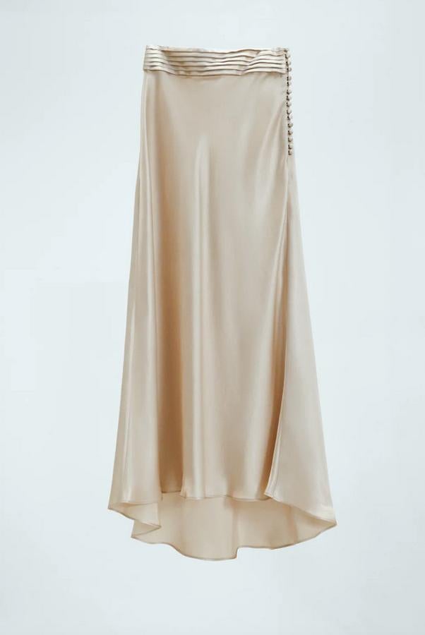 Con detalle de pliegues en la cintura y bajo asimétrico, esta falda midi satinada con cierre lateral de botones forrados a tono cuesta 49,95 euros y está disponible entre las tallas XS y L.