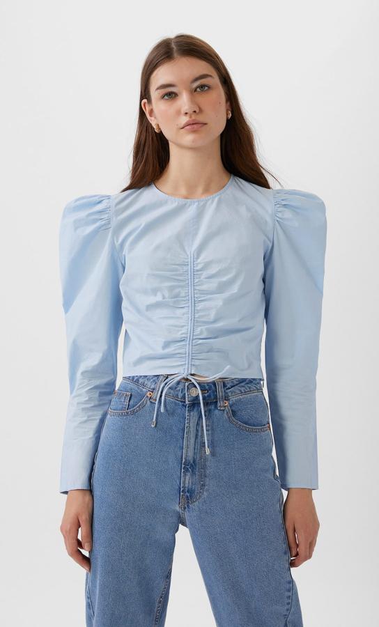 Esta blusa en popelín y azul celeste viene con diseño cropped, mangas largas y lazada en el frontal con efecto drapeado. Cuesta 7,99 euros (antes 17,99 euros) y está disponible en las tallas S, M y L.