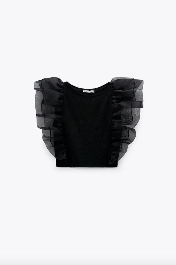 En color negro, este top de cuello redondo y manga sisa viene con detalle de volantes combinados a tonos en organza sobre los hombros. Cuesta 15,95 euros y está disponible entre las tallas S y L.