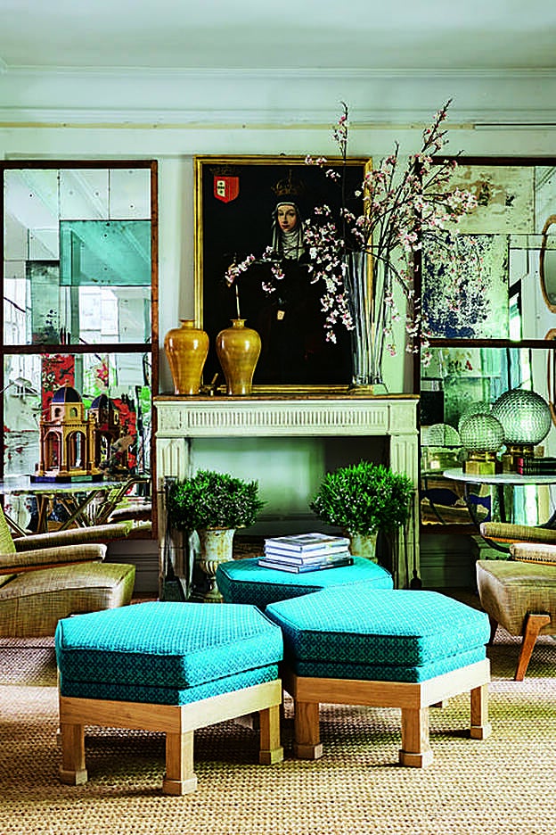 Sobre una chimenea francesa del siglo XVIII se apoya un cuadro antiguo de Santa Isabel de Portugal. El templete de madera que se refleja en el espejo de la izquierda es de José Pan de Soraluce. Las butacas son de los 70, en contraste con los pufs turquesa.