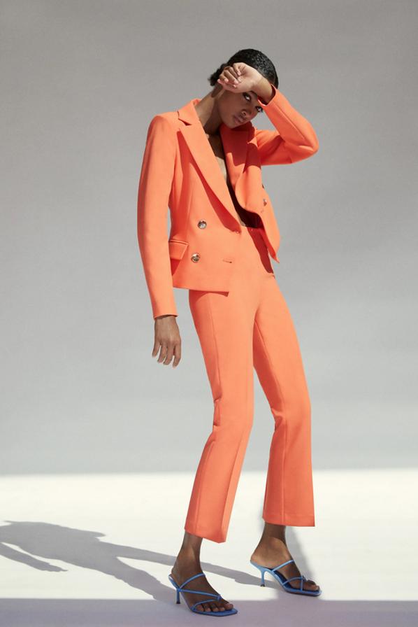 Con una blazer cruzada de diseño cropped con cierre frontal cruzado con botones metálicos (49,95 euros) y un pantalón de tiro alto con cintura interior elástica (25,95 euros) este traje en color mandarina pertenece a la colección sostenible de Inditex.
