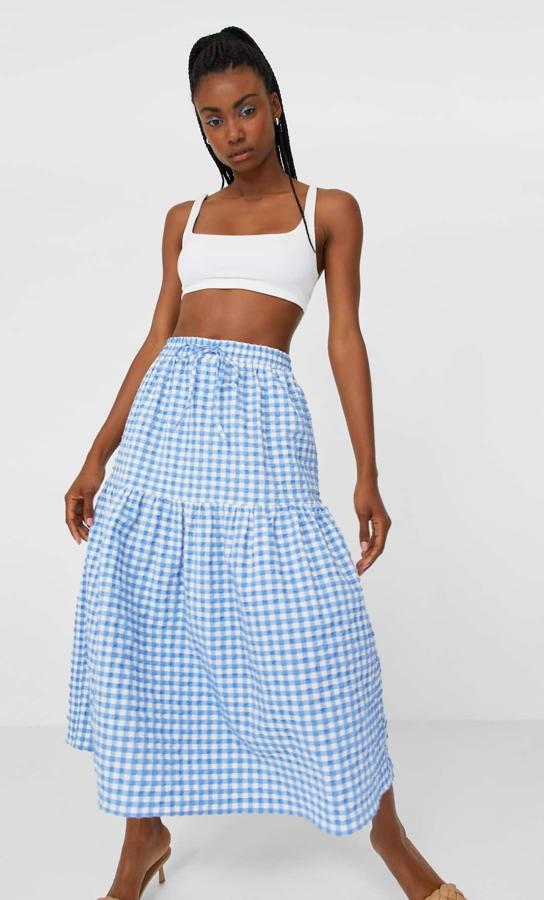 En Stradivarius hemos encontrado esta bonita falda con estampado de cuadro vichy en azul celeste, tiro alto y lazadas ajustables en la cintura. Cuesta 19,99 euros y está disponible entre las tallas XS y XL.