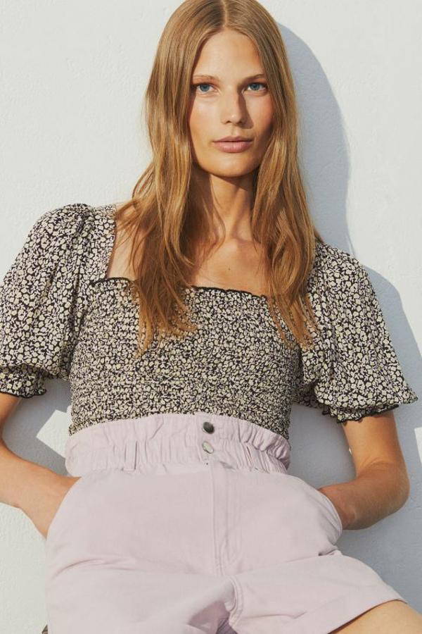 Diseño entallado en viscosa vaporosa para esta blusa negra con estampado de flores blancas y cuerpo fruncido. El escote es cuadrado y viene con mangas cortas abullonadas con remate de volante. Cuesta 19,99 euros y está disponible entre las tallas XS y XXL.