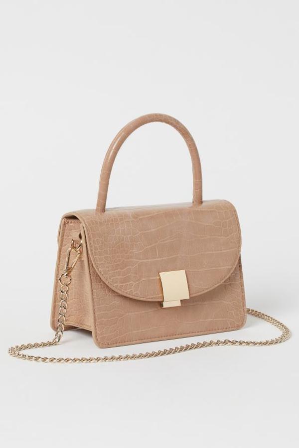 Para las que buscan un bolso de mano que pegue con todo H&M tiene en su web este bolso de piel sintética con efecto piel de cocodrilo, asa en la parte superior a tono y asa extraible de cadena de metal. Con solapa con cierre de metal, cuesta 24,99 euros.