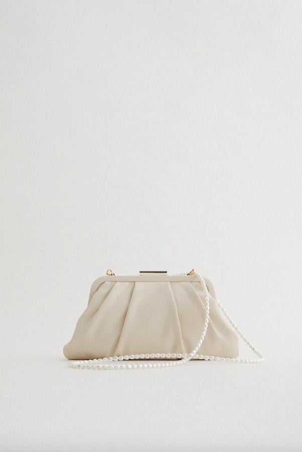Con asa de hombro de perlas para convertirla en la más elegante de las bandoleras, este bolso formato mino en blanco crudo tiene un cuerpo con detalle de pliegues e interior forrado con efecto satinado y bolsillo. Con cierre de pieza metálica, cuesta 25,95 euros.