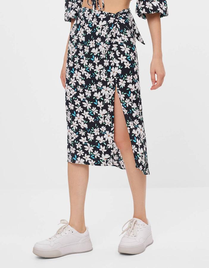 Con estampado de flores blancas sobre fondo negro, lazada en la cintura a tono y abertura en el lateral frontal, esta falda midi es de Bershka, tiene un precio de 19,99 euros y está disponible entre las tallas XS y L.