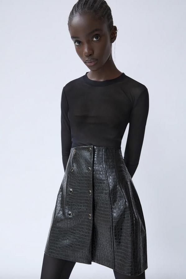 En Zara hemos encontrado esta falda mini en color negro con efecto piel de cocodrilo y cierre frontal con botones metálicos a presión. Cuesta 25,95 euros y está disponible entre las tallas XS y L.
