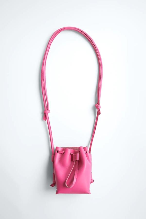 En color rosa fucsia, este bolso formato mini saca cuenta con asa de hombro tubular con detalle de nudos y cierre mediante fruncido. Es de Zara y tiene un precio de 29,95 euros.