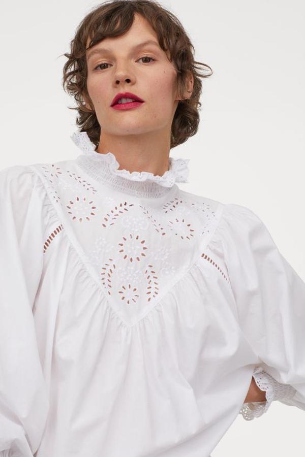 Otra propuesta perfecta para las amantes de las blusas blancas es este modelo confeccionado en popelina de algodón con efecto frufrú viene con cuello alto fruncido con bordado de encaje y canesú en V con bordado inglés delante. Las mangas tres cuartos acaban en puños anchos fruncidos con ribete de encaje bordado y el bajo está redondeado. Tiene un precio de 39,99 euros y está disponible entre las tallas XS y XL, pero solo se vende en la web de H&M.