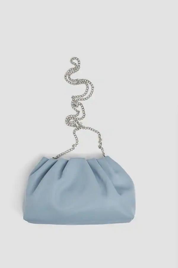 Con detalle de frunces, cierre de imán y asa larga de cadena, esta bandolera de compartimento único de Pul&Bear está disponible en azul claro, blanco y negro y tiene un precio de 15,99 euros.