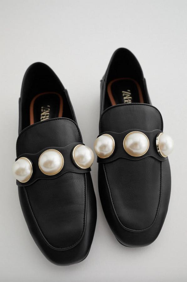 Con detalle de maxi perlas en el empeine, estos mocasines de Zara en color negro con talón pisado cuestan 29,95 euros y están disponibles entre los números 35 y 42.