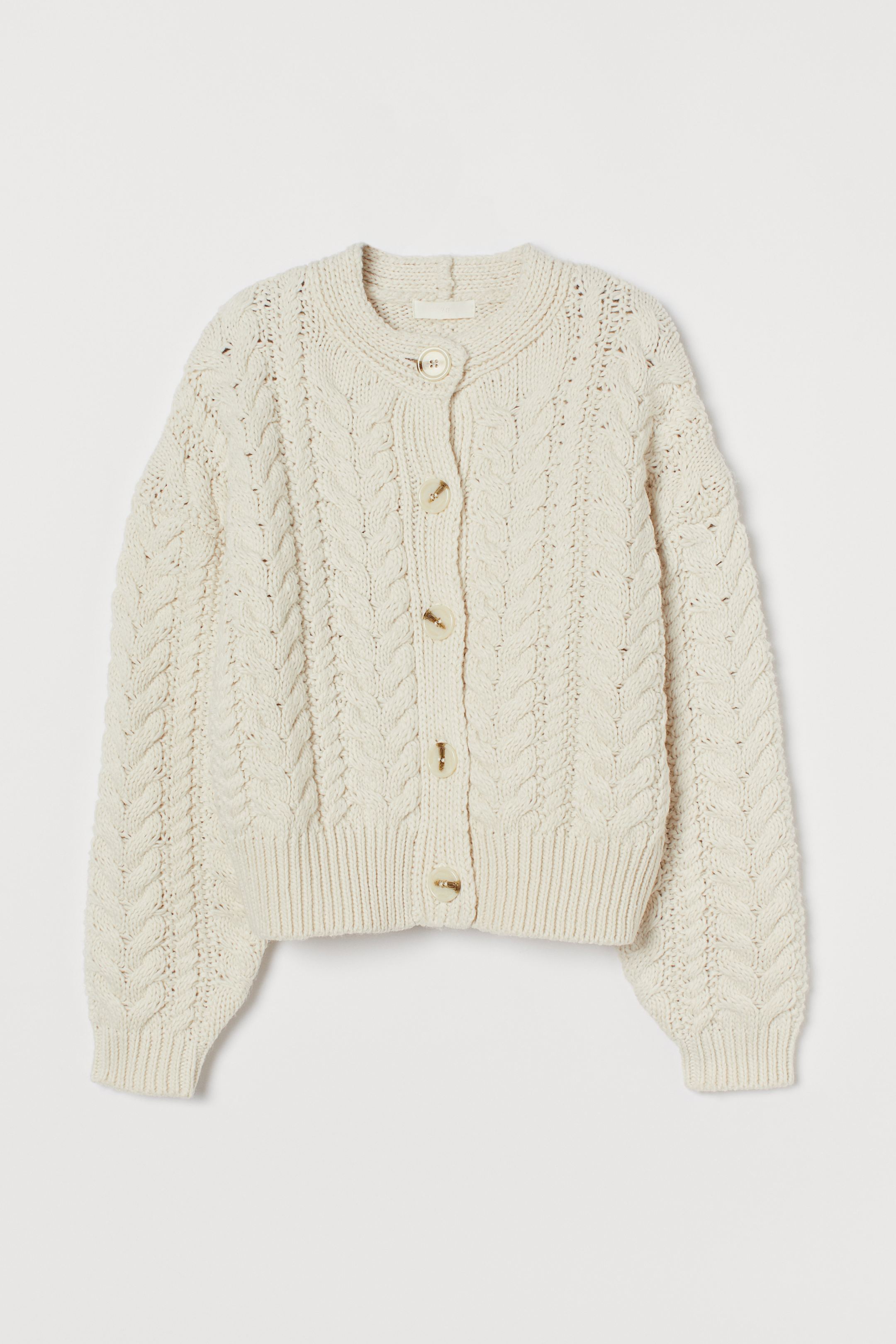 Cárdigan de punto grueso en color blanco roto con cierre de botones de la nueva colección de H&M. Ideal para combinar con vaqueros, con pantalones o con faldas mini o midi. (34,99 euros).