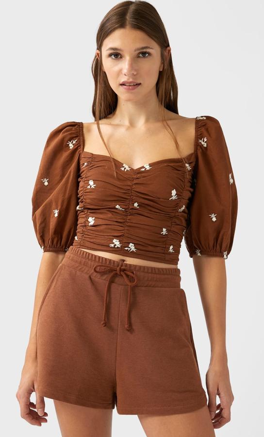 Este top en color camel oscuro con pequeñas flores bordadas en color blanco cuenta con fruncido en la parte del escote, con forma de corazón. Tiene un precio de 13,99 euros.