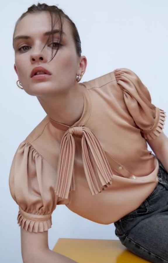 De manga corta, este modelo de blusa con lazada de Zara es diferente. Con detalles plisados, de raso y un rosa empolvado muy especial (22,95 euros).