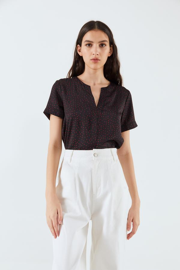 Con manga corta, cuello de pico y estampado de topos rojos sobre fondo negro, esta blusa de Sfera tiene un precio de 13,99 euros y está disponible entre las tallas S y XL.