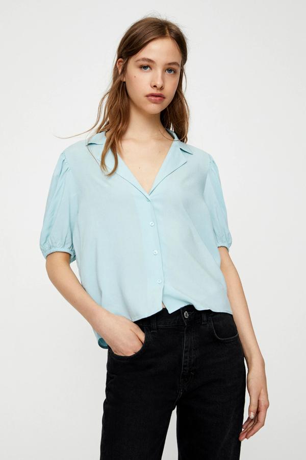 Esta camisa azul (también está disponible en rosa, crudo o negro) de manga corta con detalle de volumen cuenta con escote de pico y tiene un precio de 9,99 euros.