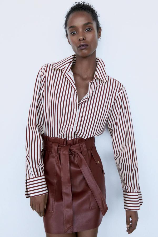 En color granate, esta falda mini efecto piel de corte paperbag cuenta con cintura elástica y cinturón a tono. Es de Zara y tiene un precio de 22,95 euros.