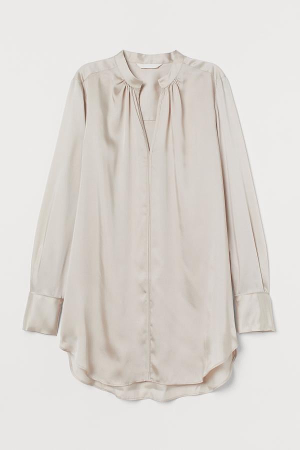 H&M nos propone esta blusa larga de satén en color beige. Con cuello elevado corto con fruncido y abertura de pico delante, cuenta con puños anchos con botón y bajo redondeado. Está disponible también en negro, blanco o rosa, y tiene un precio de 19,99 euros.