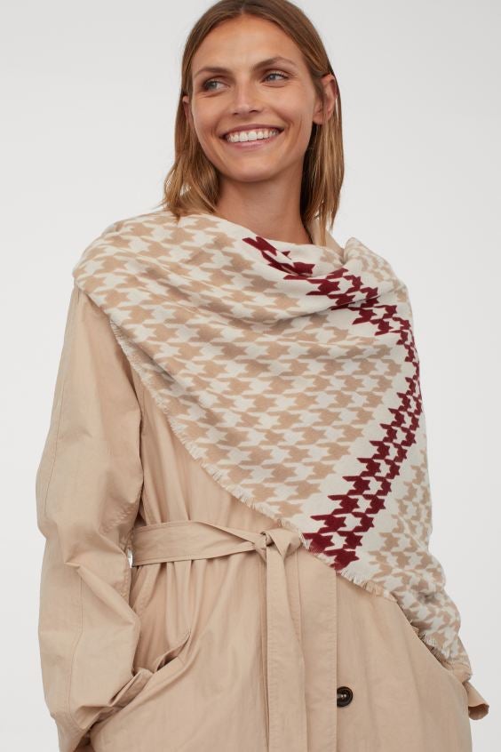 En H&M hemos encontrado este pañuelo con estampado pata de gallo en tonos beige y rojo. Confeccionado en tejido vaporoso y con acabados desflecados, tiene un precio de 14,99 euros.
