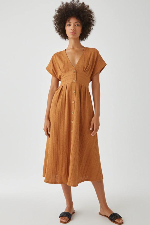 En color teja, este vestido midi en tejido con textura de manga corta está confeccionado en algodón. Con botones en la parte delantera, tiene un precio de 22,99 euros.