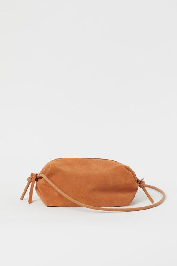 En ante suave con detalles de piel sintética, este bolso de H&M en color naranja viene con correa fina ajustable con nudos en los extremos, cremallera superior y forro de satén en poliéster reciclado. Cuesta 29,99 euros y es perfecto para poner una nota de color en tus estilismos.