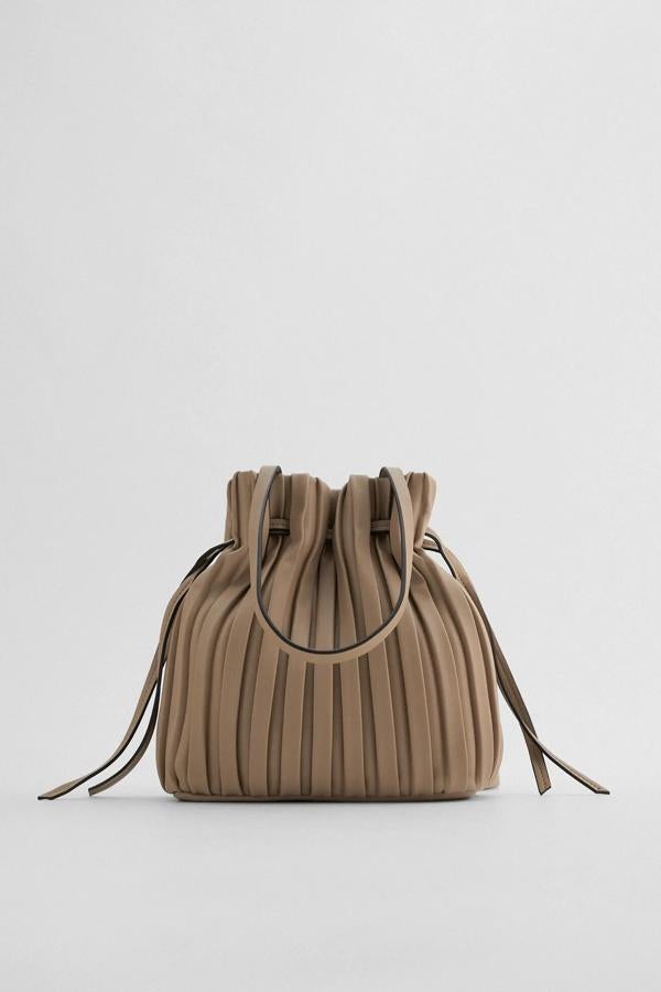 En color gris y disponible en varios colores, este bolso formato mini cuenta con cuerpo plisado con detalle de fruncido en la parte superior. Con asas de hombro ajustable, es de Zara y tiene un precio de 19,95 euros.