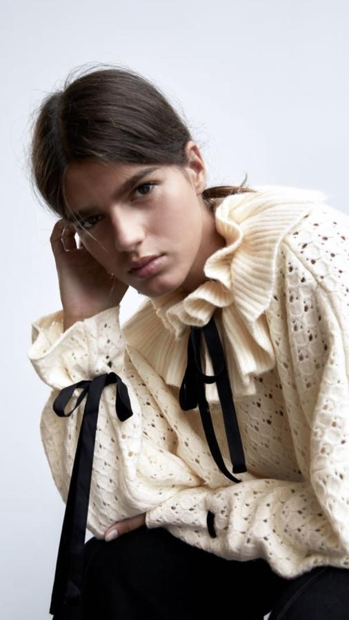 Jersey de punto calado en color crudo, con detalles de cinta negra y volantes en el cuello, de Zara (25,95 euros).
