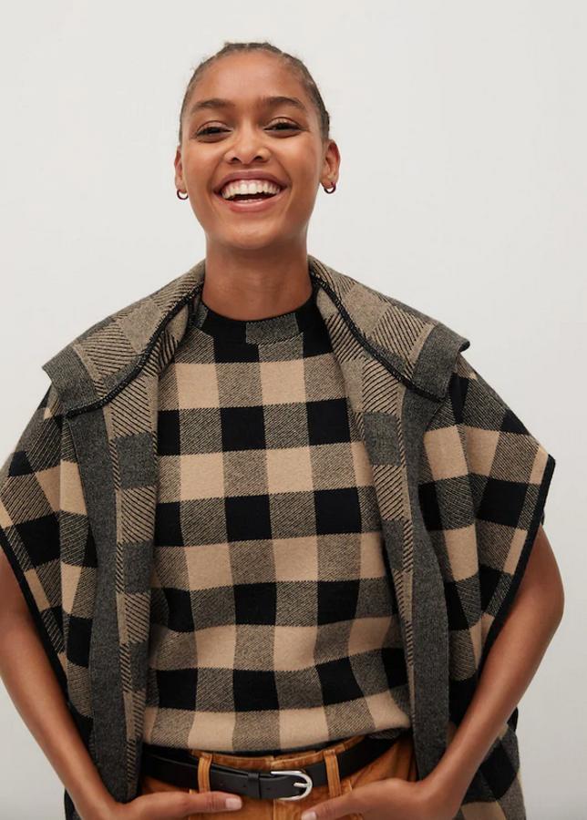 Con estampado de cuadros en marrón medio y negro, esta capa de punto de Mango es de diseño ancho, diseño midi, manga corta y capucha. Con bolsillos laterales, tiene un precio de 59,99 euros y está disponible en las tallas S, M y L.