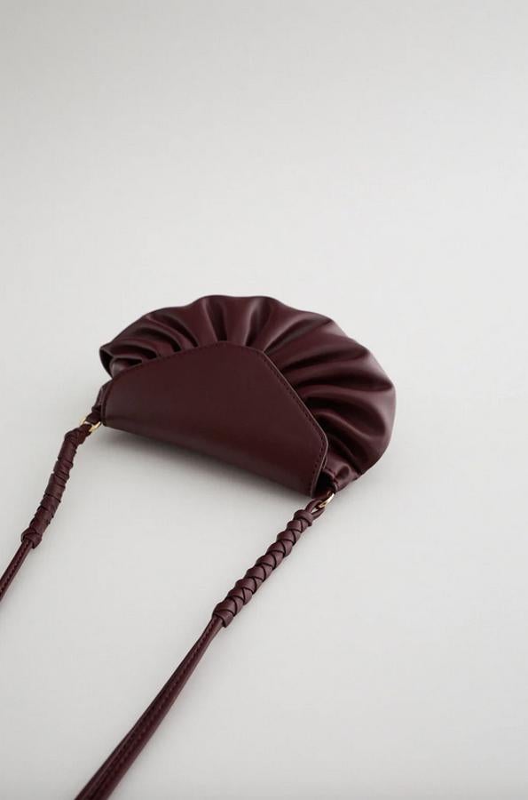 Con cuerpo fruncido y asa de hombro de bandolera con detalles entrelazados, esta bandolera granate de Zara viene con cierre de imán y de 19,95 euros ha pasado a costar 9,99 euros. También está disponible en azul.