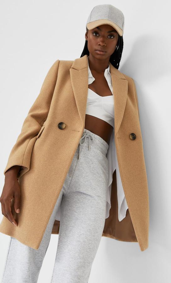 De cuello y solapa con manga larga, este abrigo básico de paño de Stradivarius en color camel viene con bolsillos delanteros con solapa y cierre frontal cruzado con botones de carey. Tiene un precio de 49,99 euros y está disponible entre las tallas S y XL.