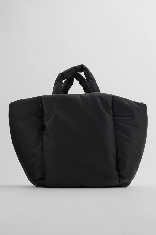 En color negro, este bolso formato shopper con cuerpo y asas de mano acolchadas cuenta con bolsillo en la parte delantera y asa de hombro función bandolera.