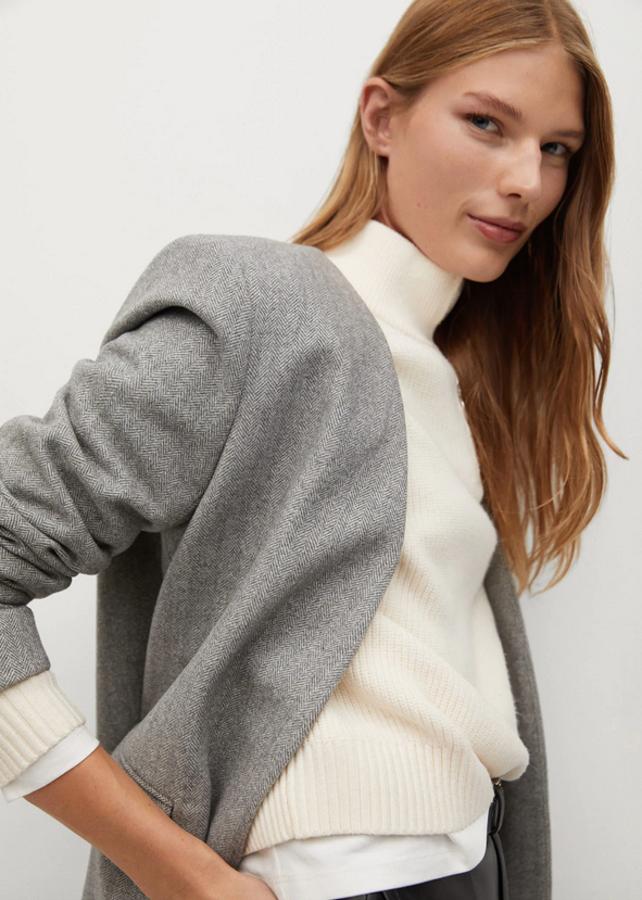 Cuello de pico sin solapa para esta americana de lana con diseño estructurado de Mango. Con puños abotonados y bolsillos de solapa laterales, tiene un diseño de espiga en gris claro, cuesta 69,99 euros y está disponible entre las tallas XS y XL.