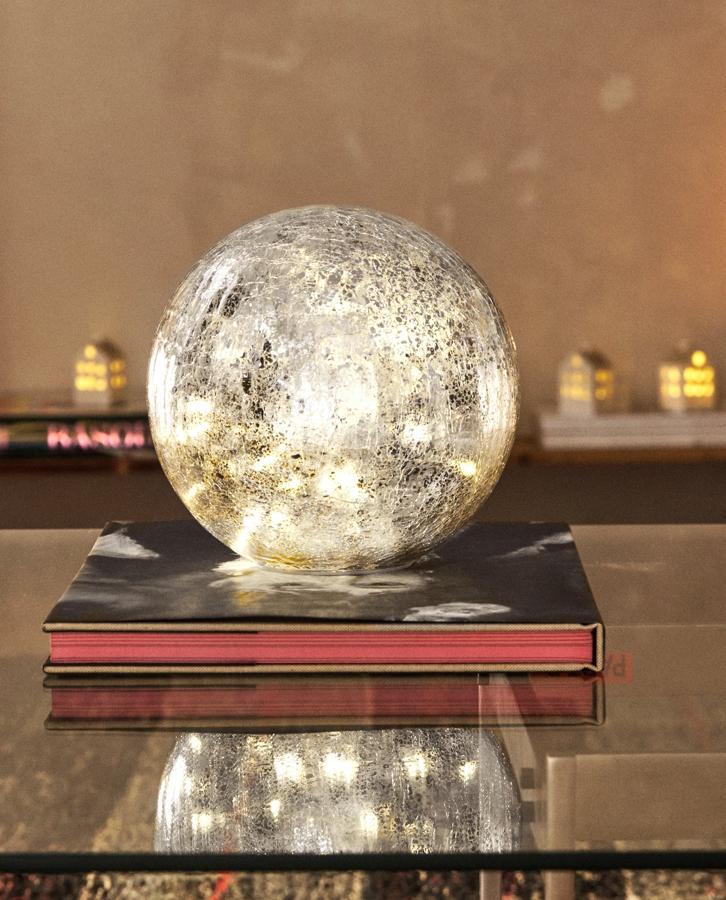 Disponible en plata o dorado, esta bola decorativa de vidrio con luz en su interior funciona con pilas y tiene unas medidas de 20x19x20 centímetros y un precio de 29,99 euros.