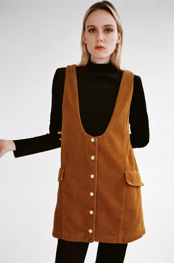 En tono whisky anaranjando, con tirantes anchos, bajo acabado en evasé y bolsillos de tapeta en delantero, este pichi de Zara en pana viene con cierre de botones metálicos en el frontal y cuesta 29,95 euros. Está disponible entre las tallas XS y L.