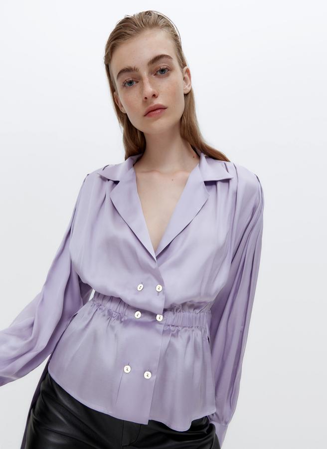 Con hombreras y botones metalizados en plata, esta camisa lila confeccionada en un tejido satinado de cupro de alta calidad viene con cierre cruzado doble, cintura elástica y cinturón a tono. De 79 euros ha pasado a costar 59,25 euros y está disponible en las tallas S, M y L.