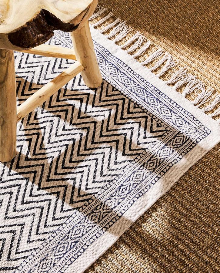 En color blanco con estampado de zigzag en tonos grises, esta alfombra de algodón con flecos tiene unas medidas de 60x120 centímetros y un precio de 29,99 euros. Está disponible también de 150x200 centímetros.