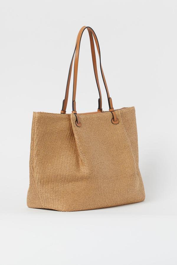 Confeccionado en paja trenzada de color beige con detalles en piel sintética, este bolso shopper con dos asas y compartimento interior con cremallera es de H&M y tiene un precio de 19,99 euros.