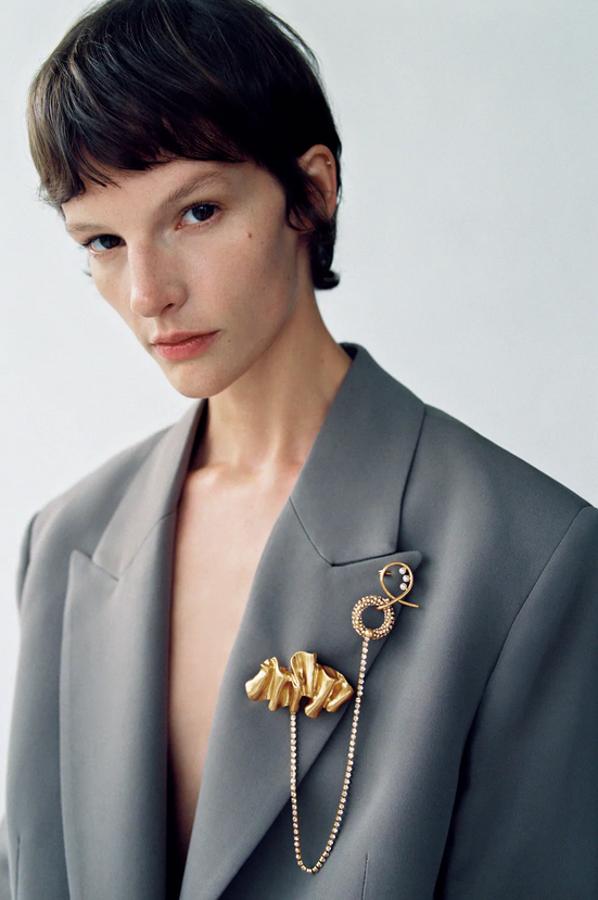 Con cadena, aplicación de brillos y perlas, este broche dorado de Zara tiene un precio de 12,95 euros.