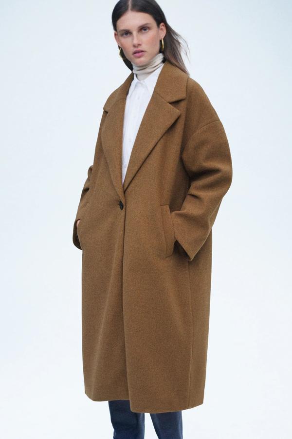 En color tostado, este abrigo amplio con manga abullonada con pliegues y bajo acabado con abertura en la espalda es de Zara y tiene un precio de 49,95 euros. También está disponible en beige, gris claro y gris oscuro