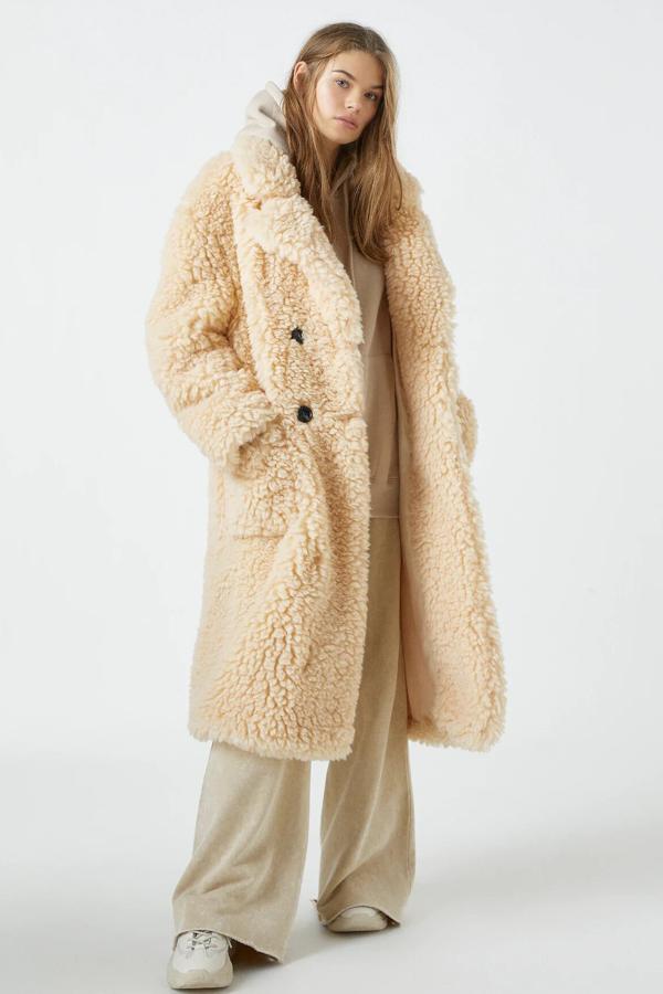 Este abrigo largo de pelo rizado en color crudo cuenta con cierre mediante botones y bolsillos de plastrón. Es de Pull & Bear y tiene un precio de 49,99 euros.