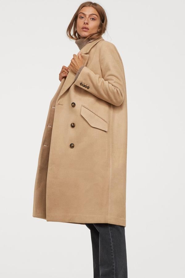 En color beige, este abrigo largo de doble botonadura con botones decorativos en los puños y abertura en la parte trasera es de H&M y tiene un precio de 59,99 euros.