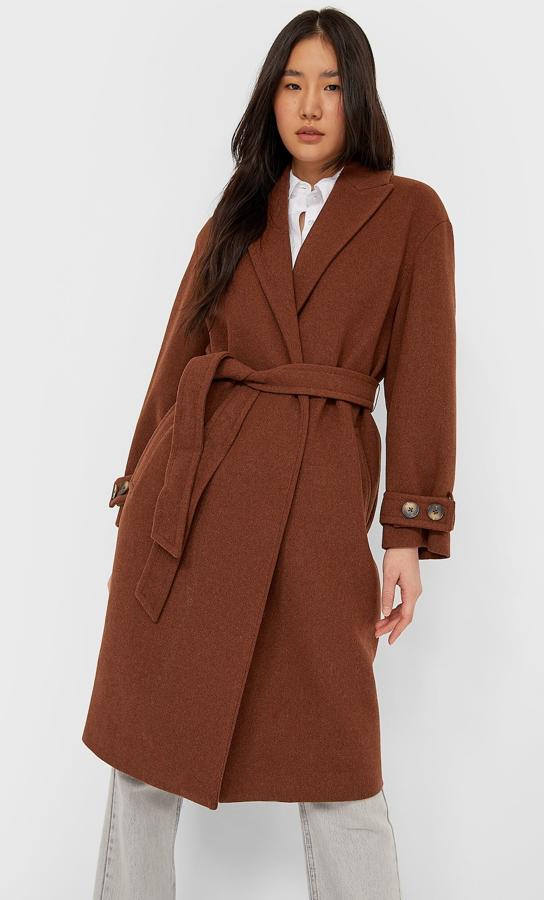 Disponible en varios colores, este abrigo marrón con detalle de cinturón del mismo tono es de Stradivarius y tiene un precio de 59,99 euros.