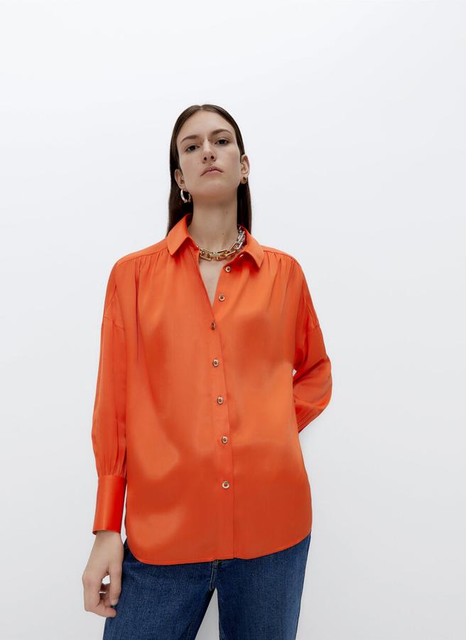 Confeccionada en tejido satinado, esta camisa con cuello clásico y botones ocultos con tapeta viene con detalle de rizo en canesú delantero. De diseño oversize y color naranja, podemos encontrarla en las tallas S y M por 79 euros.