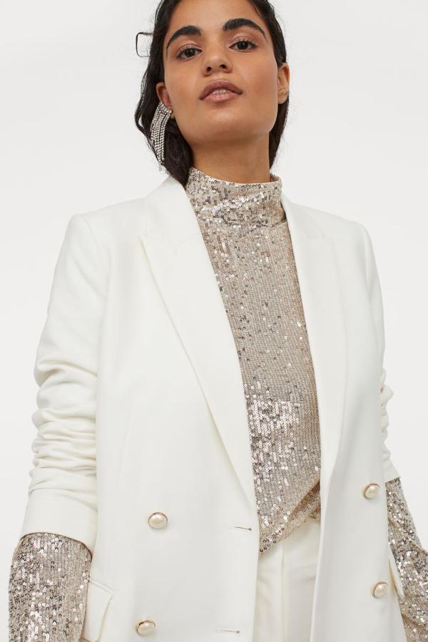 Blusa en malla bordada de lentejuelas con ligero vuelo, manga larga y cuello elevado. Lleva una abertura de pico en la espalda con botones ocultos en la nuca y los hombros caídos. El forro que lleva está confeccionado con poliéster parcialmente reciclado. (H&M, 29,99 euros)