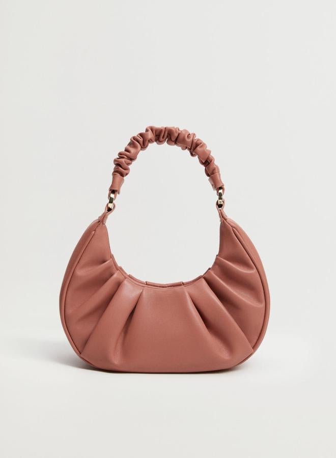En color coral, este bolso pequeño con diseño redondeado y detalles fruncidos cuenta con dos asas, una corta y una larga ajustable, y tiene un precio de 19,99 euros.