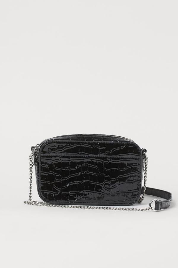 Este minibolso en piel sintética y formato bandolera de H&M con efecto piel de cocodrilo en negro acharolado viene con cadena de metal y correa a tono. Con dos compartimentos que se cierran con cremallera, cuesta 14,99 euros.